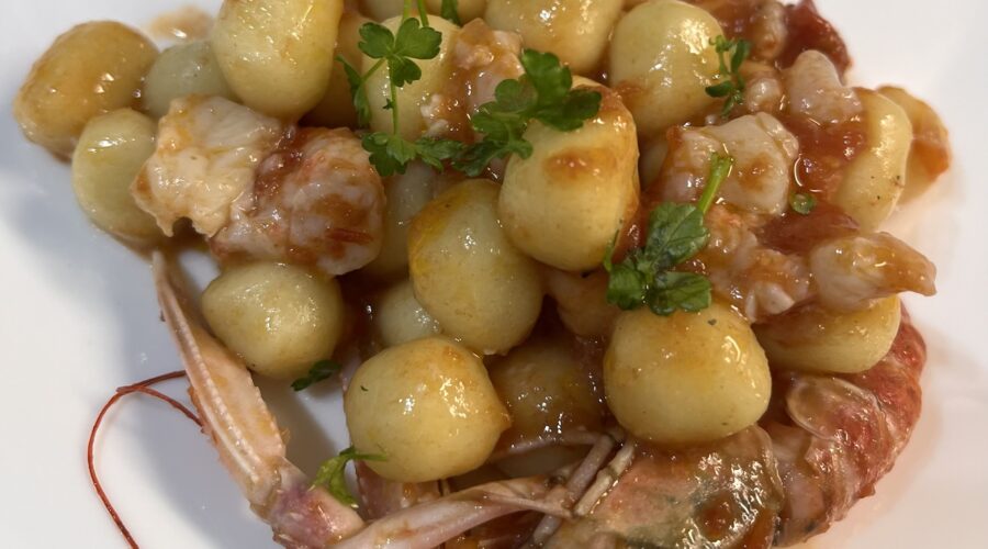 Chicche di patate condite con sugo di pomodoro e scampi, guarnite con prezzemolo fresco